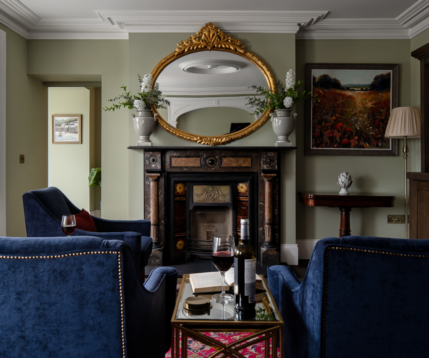 A green living room with blue seats, a mirror and a brown fireplace.