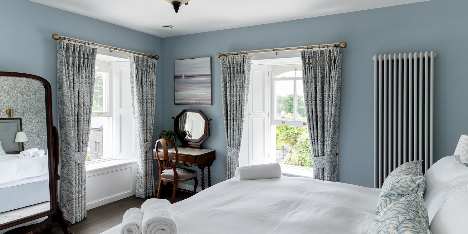 A blue bedroom with two windows and a double bed.