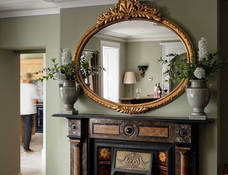 An olive green room with a mirror and a dark brown fireplace.