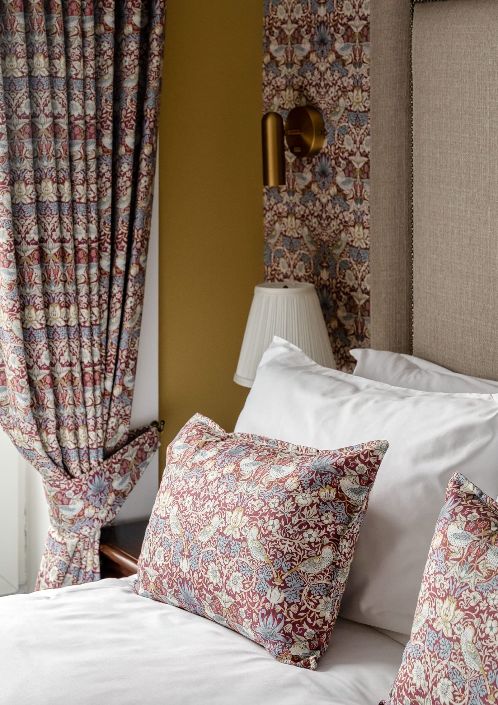 Patterned pillows on a bed next to matching curtains and a bedside lamp.