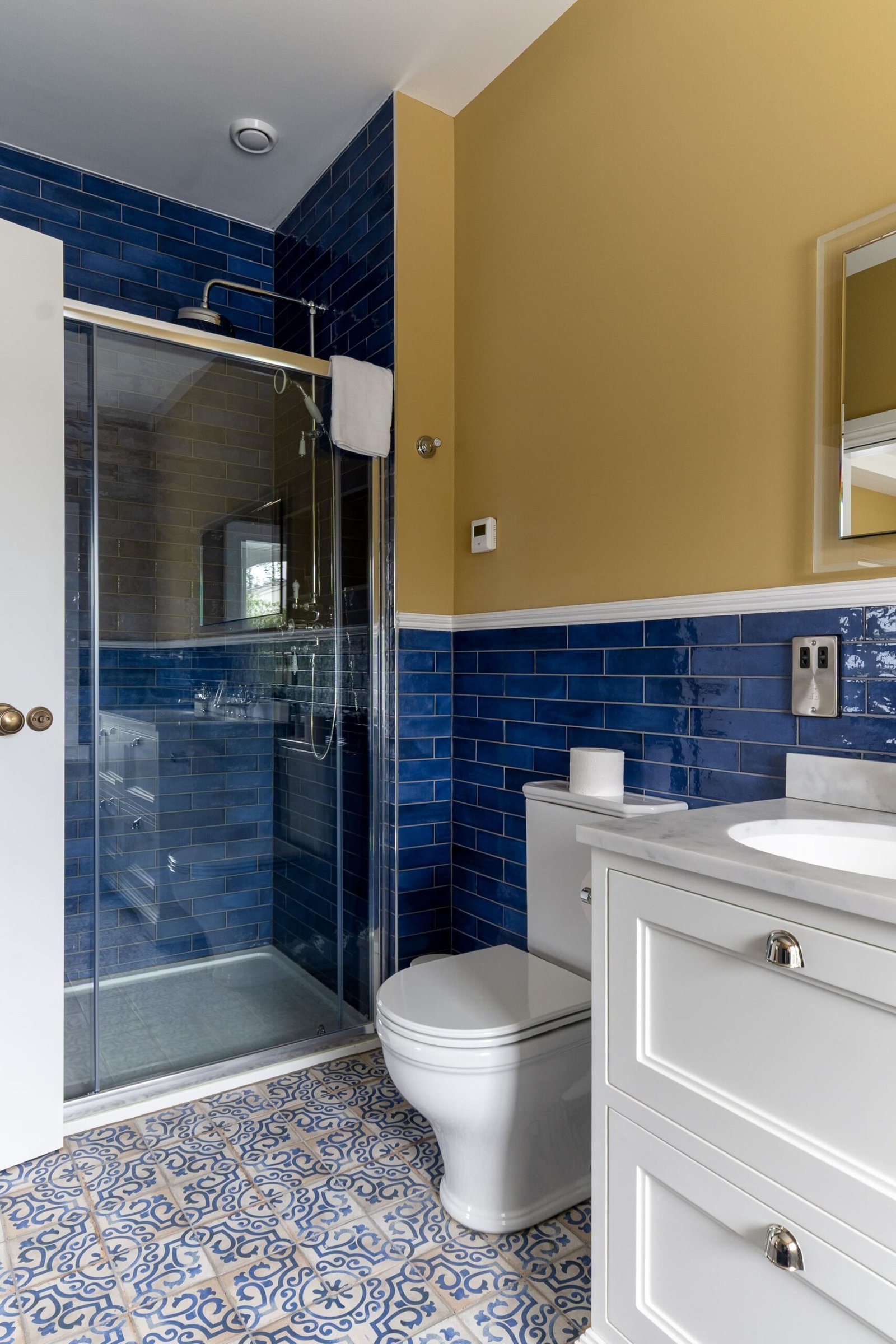 A white toiler and sink in a bathroom with blue tiles and yellow walls.