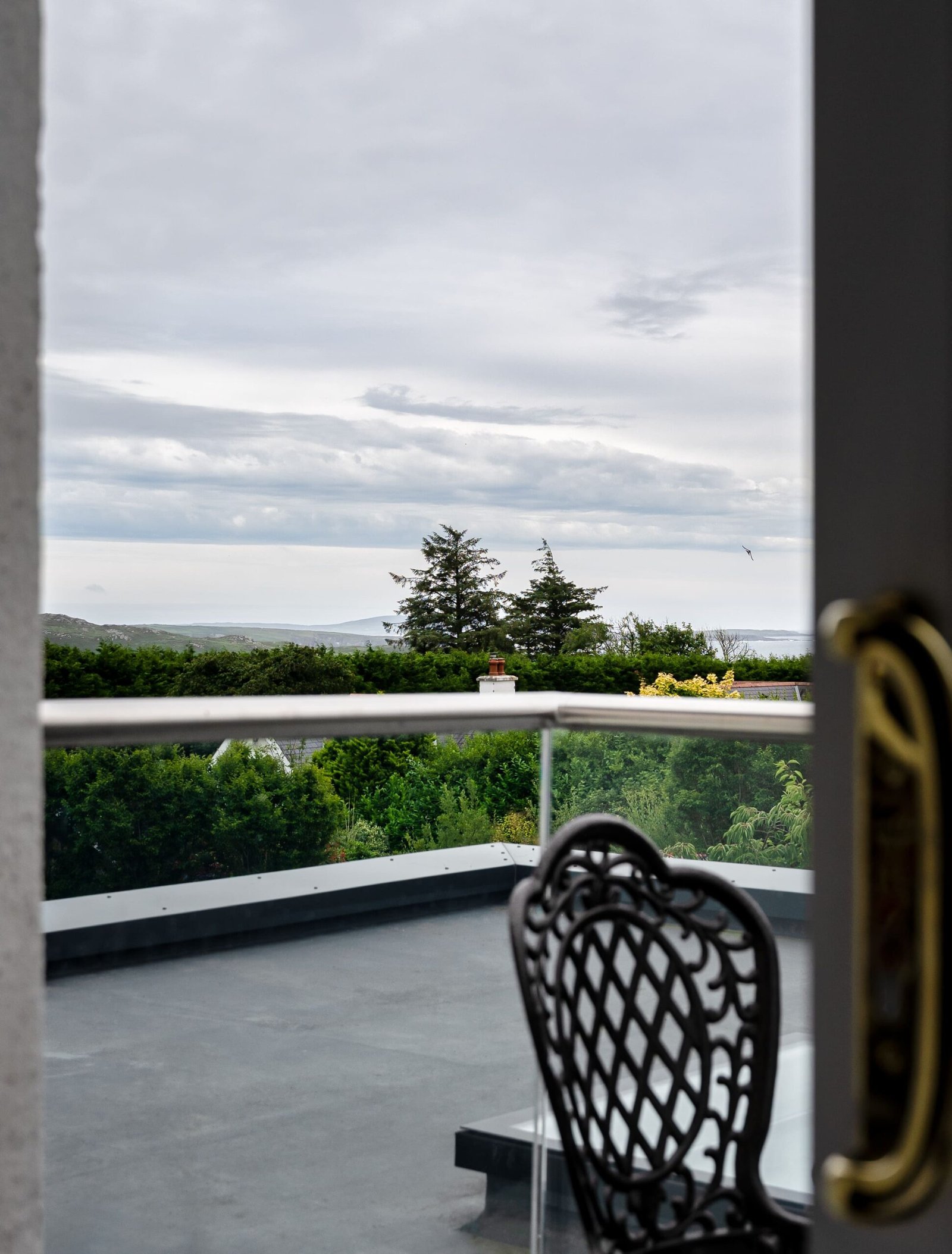A view from a balcony looking out over trees and distant hills.