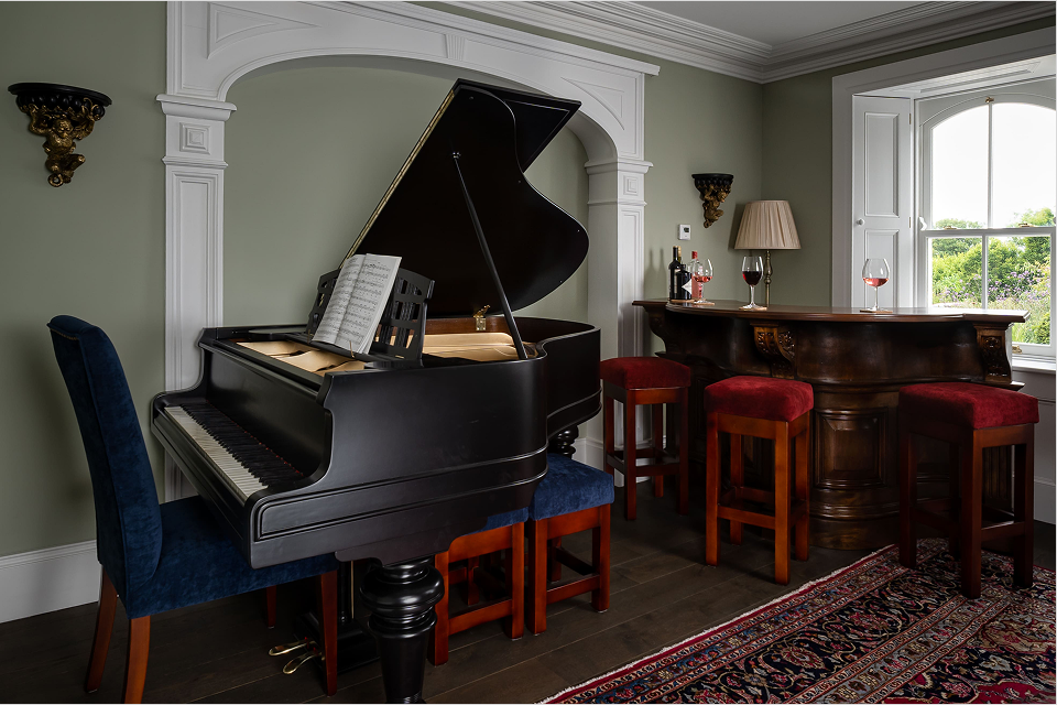 A piano in an olive green room with dark brown wooden flooring.