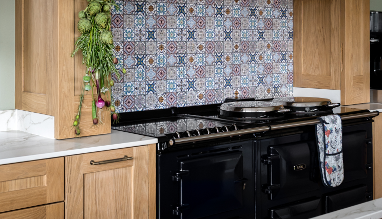 A large black stove in a kitchen with patterned wall tiles and wooden cabinets.