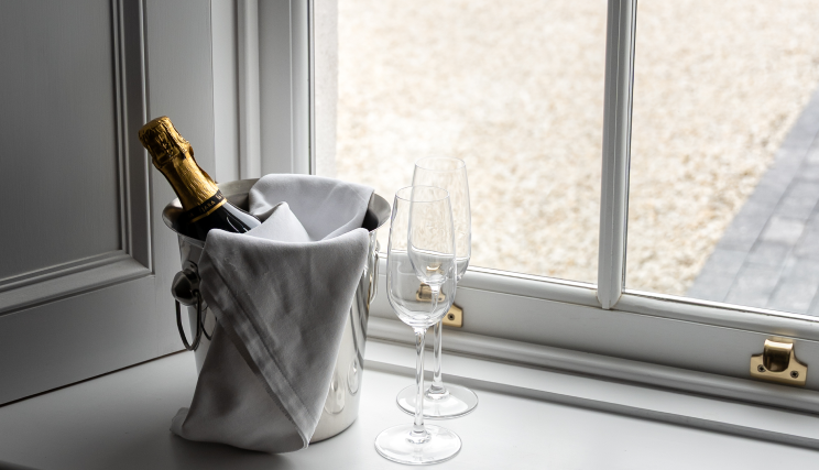 A close up of champagne with two glasses by a window.