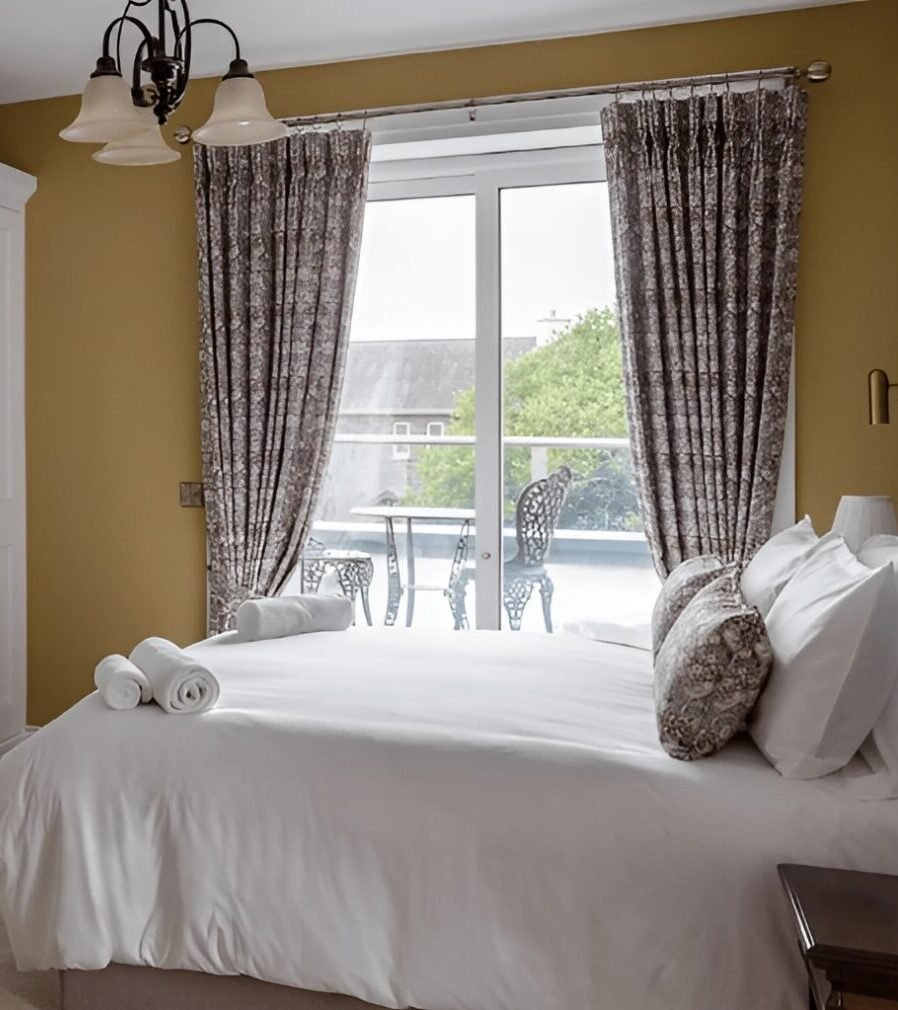 A yellow bedroom with a double bed and patterned curtains.